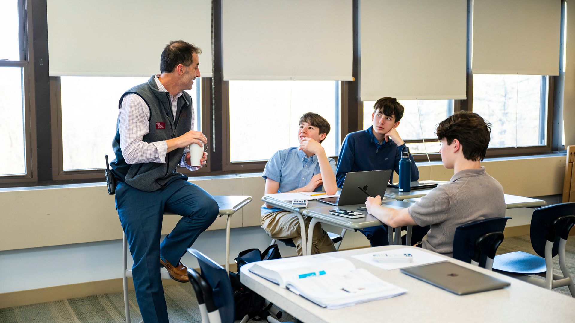 A teacher with students at SLS. Your teachers won’t stand at the front of the room and lecture. They’ll pull up a chair beside you, ask tough questions, and nudge you out of your comfort zone.